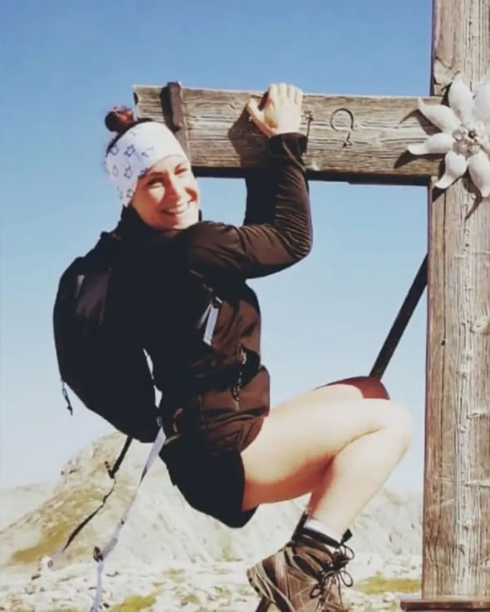 Woman smiling while climbing wooden cross on Austrian mountain, related to boyfriend who abandoned her and horrible message after body found