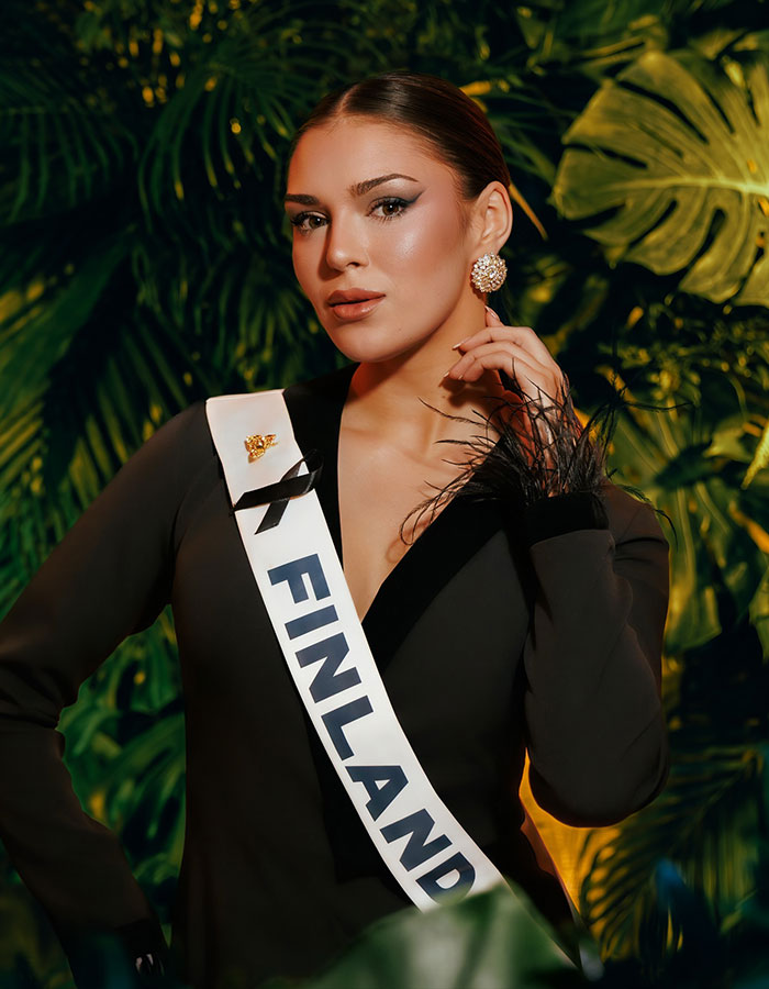 Miss Finland wearing a sash posing confidently amid tropical leaves, linked to controversy and losing her crown. Miss Finland wearing a sash posing confidently amid tropical leaves, linked to controversy and losing her crown.