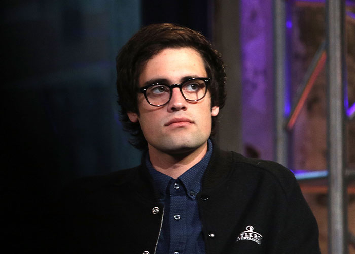 Young man wearing glasses and a dark jacket, looking thoughtful in a dimly lit setting related to Rob Reiner’s son arrest news. Young man wearing glasses and a dark jacket, looking thoughtful in a dimly lit setting related to Rob Reiner’s son arrest news.