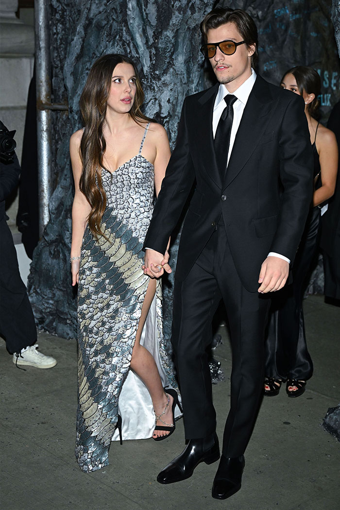 Millie Bobby Brown and Jake Bongiovi holding hands at a formal event, sparking fan theories about her arm injury. Millie Bobby Brown and Jake Bongiovi holding hands at a formal event, sparking fan theories about her arm injury.