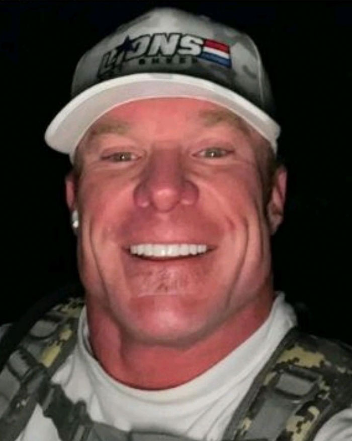 Smiling man wearing a cap and camo backpack, related to patient&rsquo;s haunting final post from dentist chair before fatal procedure.