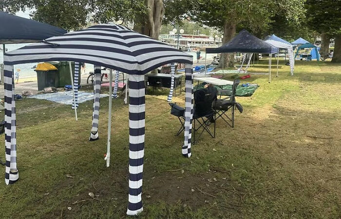 Public space reserved with striped tents and chairs on grass near waterfront, locals express outrage over New Year&rsquo;s Eve act.