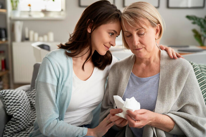 Young woman comforting older woman holding tissues, depicting emotional moments in big family drama situations at home.