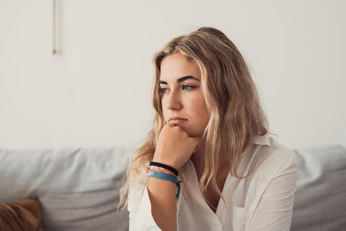 Young woman sitting on a couch looking thoughtful, illustrating small tricks that make being a grown-up easier.