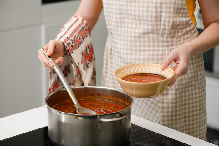 Person wearing apron serving soup from pot into bowl, demonstrating small tricks that make being a grown-up easier.