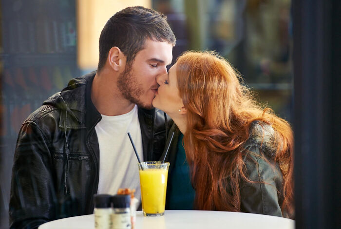 Couple kissing at a cafe table with drinks, illustrating crazy things people do to make their ex pine for them.