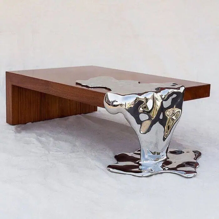 Modern wooden table with a melting silver metal leg creating a trippy, surreal visual effect in a minimalist setting.