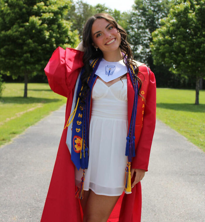 Young woman in red graduation gown standing outdoors, representing trans instructor ousted from college controversy.
