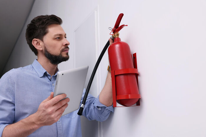 Man inspecting a red fire extinguisher on the wall while holding a tablet, related to revenge story themes and lessons.