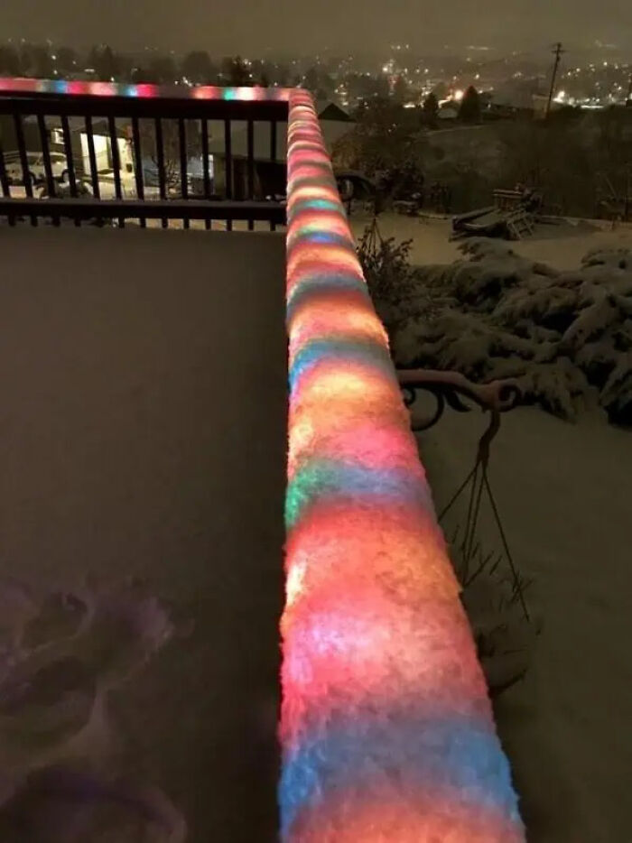 Snow-covered railing illuminated with colorful lights at night creating a trippy picture with vibrant glowing patterns.