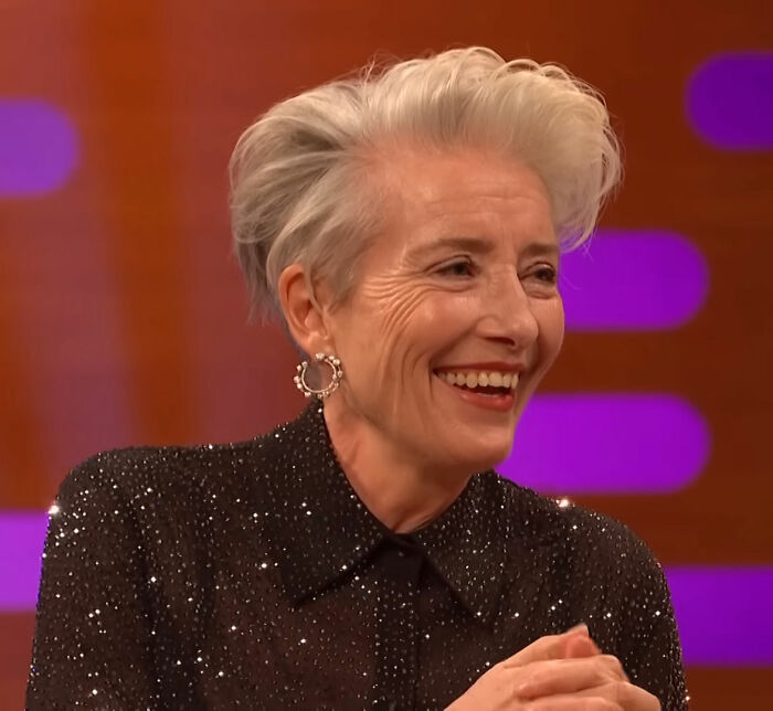 Older woman with short white hair in sparkly black top laughing during a TV interview discussing Timothée Chalamet Love Actually. Older woman with short white hair in sparkly black top laughing during a TV interview discussing Timothée Chalamet Love Actually.