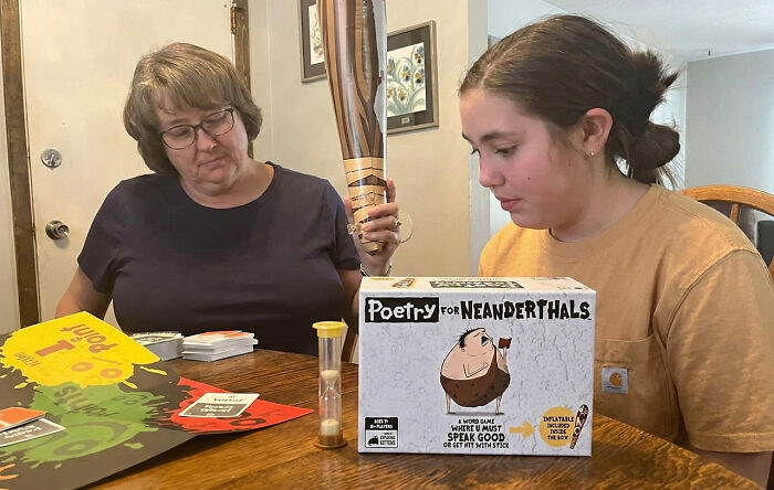 Two people playing the best party game of all time, Poetry for Neanderthals, with game cards and props on the table.