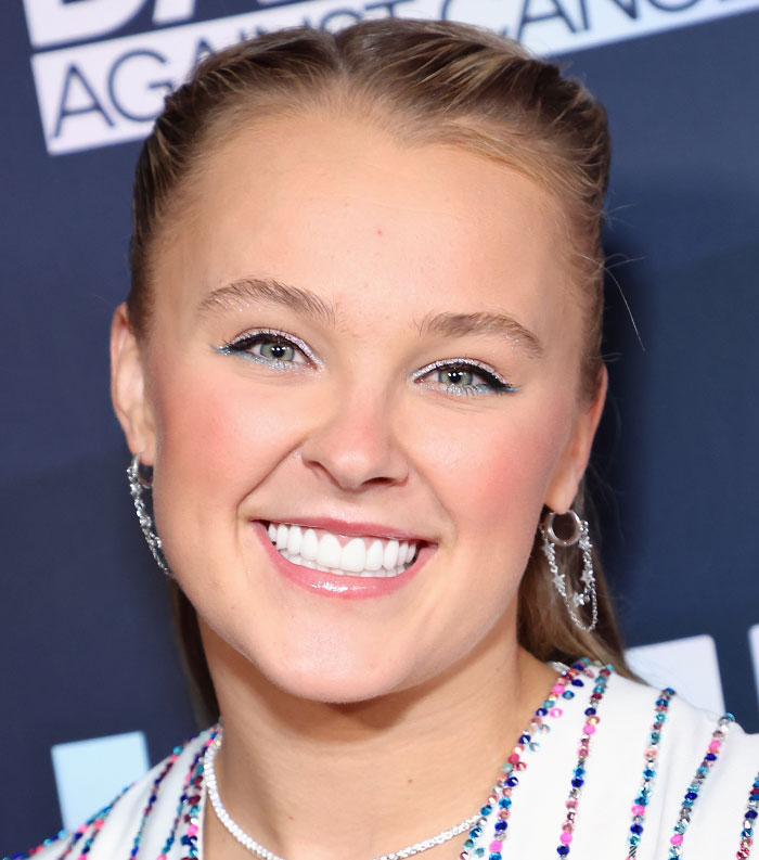 Smiling young celebrity with blue eyeliner and sparkling earrings at an event about most disliked celebrities of 2025