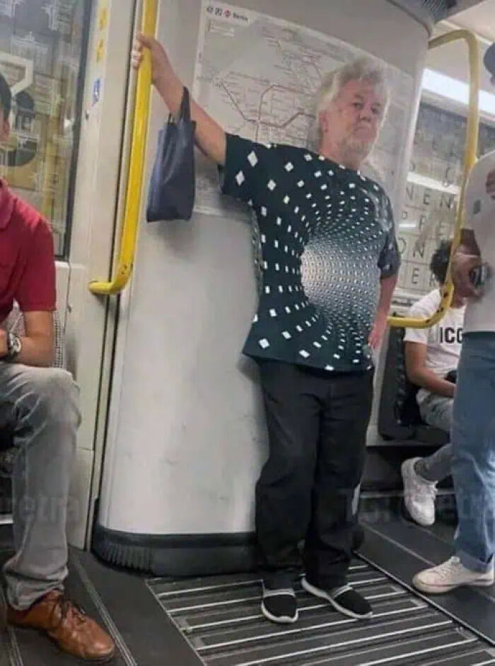 Man on a subway wearing a trippy shirt with an optical illusion vortex design creating a distorted reality effect.