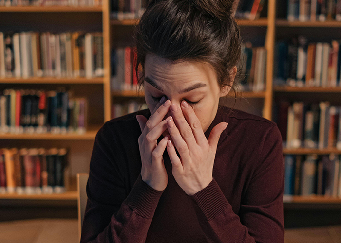 Woman in a maroon sweater rubbing her eyes, stressed in a library setting, reflecting tension with toxic mother-in-law during Christmas. Woman in a maroon sweater rubbing her eyes, stressed in a library setting, reflecting tension with toxic mother-in-law during Christmas.