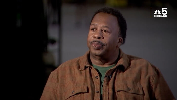 Man in a brown jacket sharing fascinating secrets about celebrities in an interview setting with a dark blurred background.