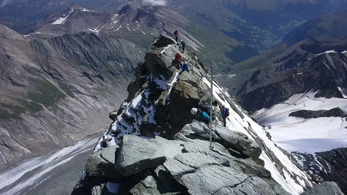 Climbers ascending Austria’s highest peak with rocky terrain and snowy patches in a remote mountainous landscape. Climbers ascending Austria’s highest peak with rocky terrain and snowy patches in a remote mountainous landscape.
