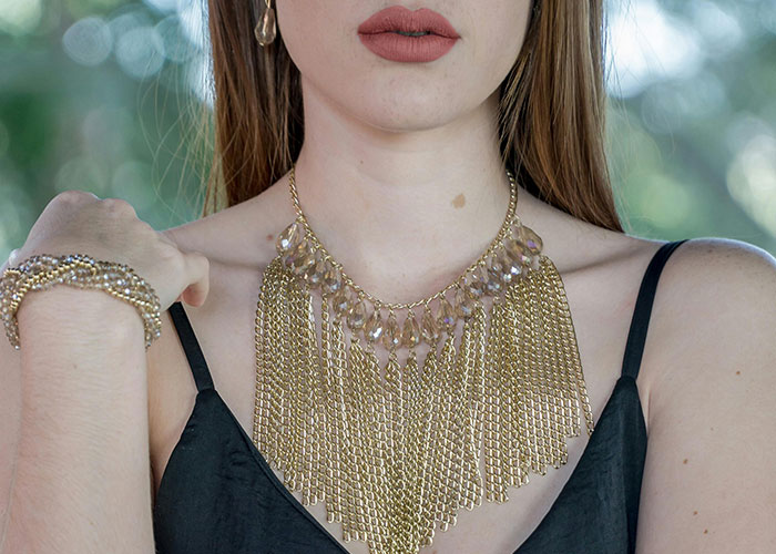 Close-up of woman wearing gold chain fringe necklace and matching bracelet, showcasing luxury accessories deemed rip-offs.
