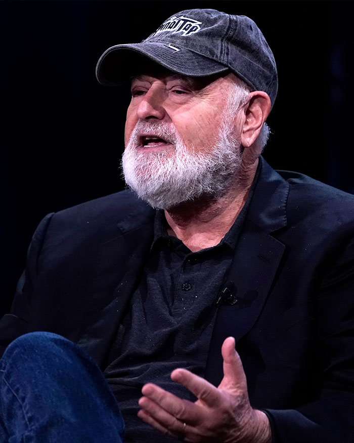 Rob Reiner speaking during an interview, wearing a black jacket, cap, and discussing the Christmas party incident.