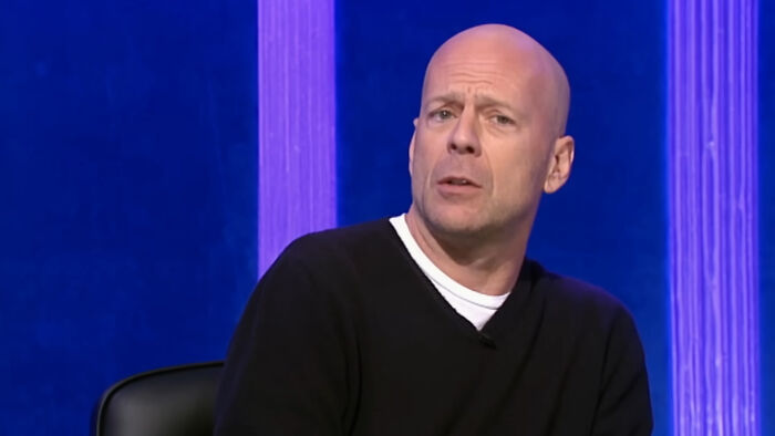 Bald man in black sweater speaking in a studio with blue and purple background, celebrities people think suffer concept.