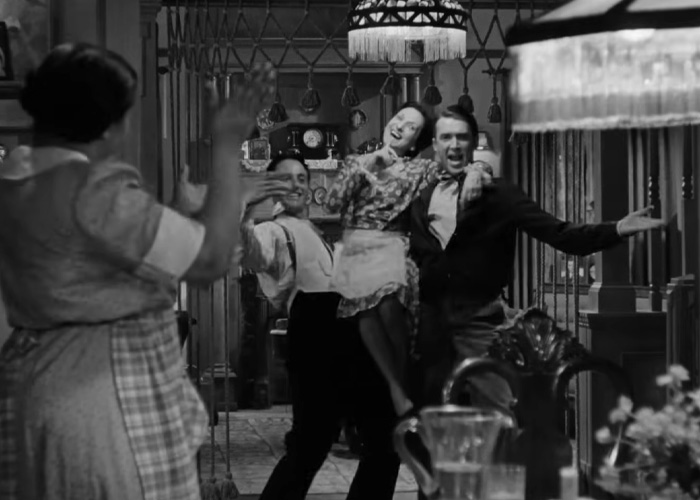 Black and white scene from a beloved Christmas classic with joyful characters dancing in a festive home setting.