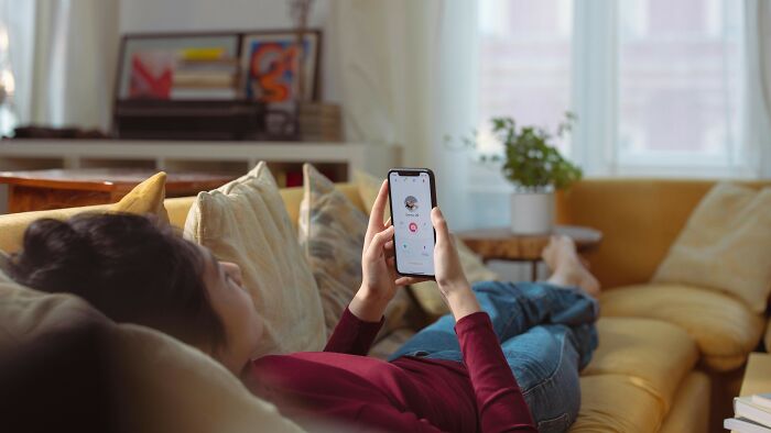 Person lying on a couch holding a phone, voting in an ambiguous situation about who is at fault or in the right.