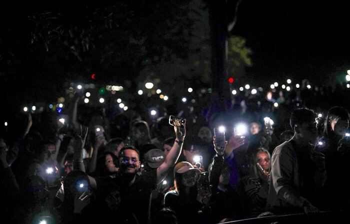Crowd holding up phones with lights on at night, illustrating public space reserved on New Year&rsquo;s Eve slammed by locals.