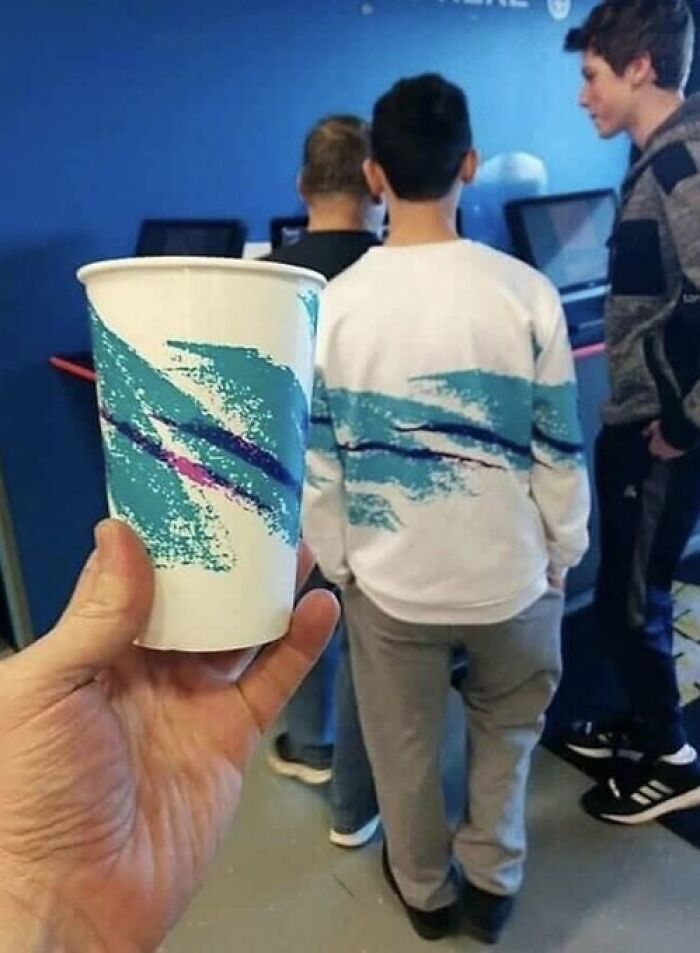Paper cup held in front of a person wearing a matching trippy picture design on their sweatshirt, creating a surreal effect.