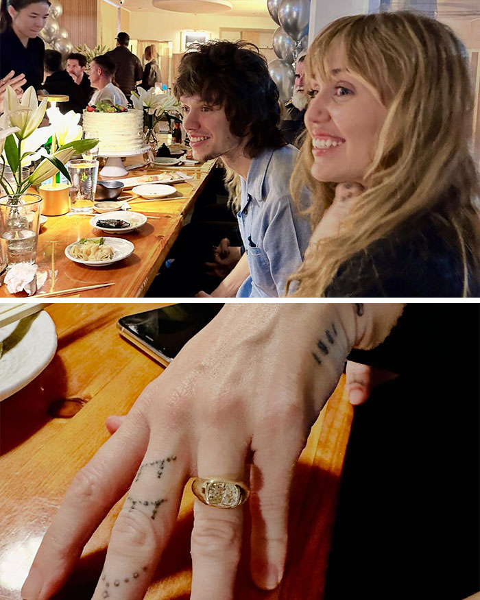 Miley Cyrus and Maxx Morando smiling at engagement party with close-up of gold ring on finger at wooden table. Miley Cyrus and Maxx Morando smiling at engagement party with close-up of gold ring on finger at wooden table.