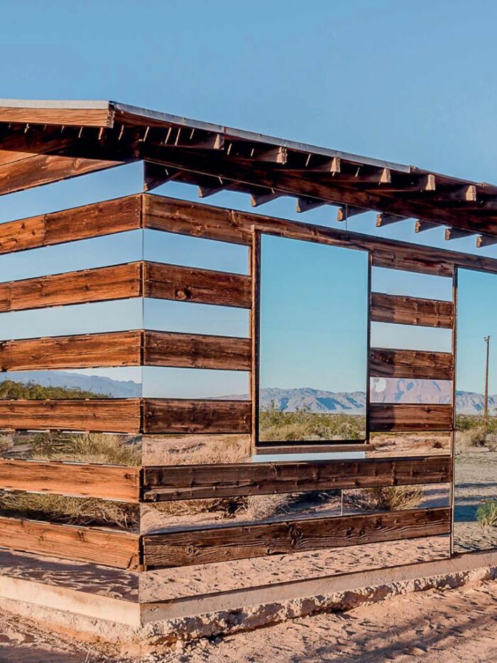 Wooden structure with mirrored panels reflecting desert landscape, creating a trippy pictures effect from another reality.
