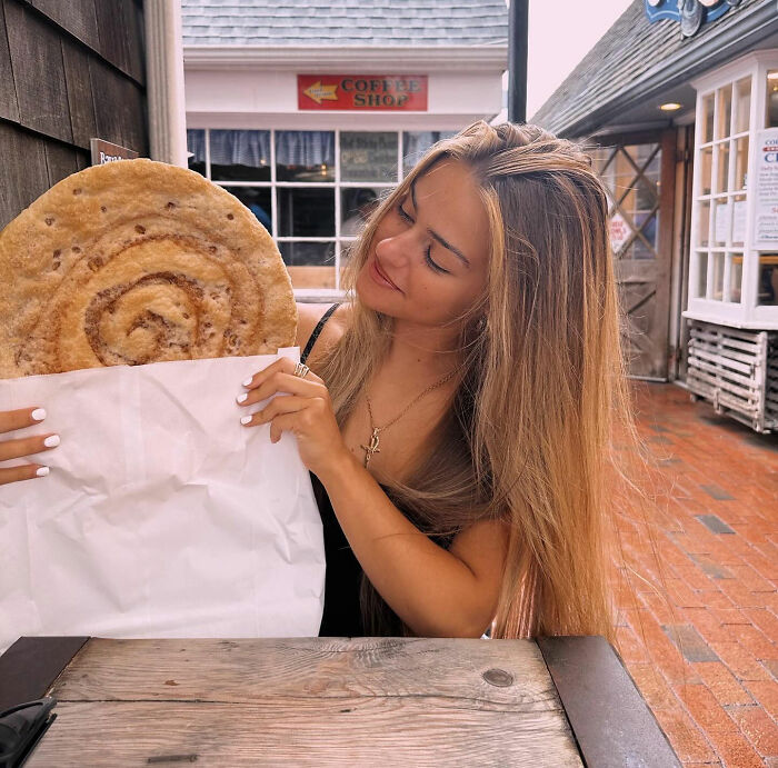 21-year-old pizza maker sitting outdoors, holding large pizza crust wrapped in paper, smiling and looking at it. 21-year-old pizza maker sitting outdoors, holding large pizza crust wrapped in paper, smiling and looking at it.