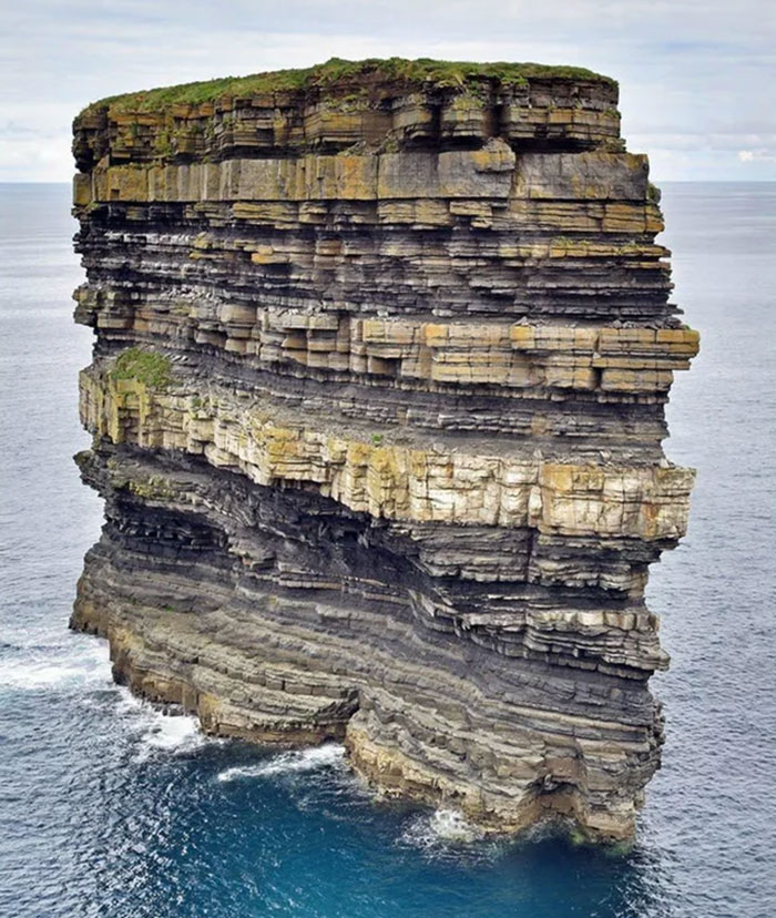 Stratified rock formation rising from ocean with layers symbolizing existence, reality, and the universe concepts in nature.