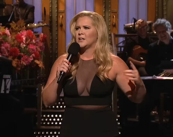 Amy Schumer performing on stage, holding a microphone and showcasing dramatic weight loss during a live comedy show. Amy Schumer performing on stage, holding a microphone and showcasing dramatic weight loss during a live comedy show.