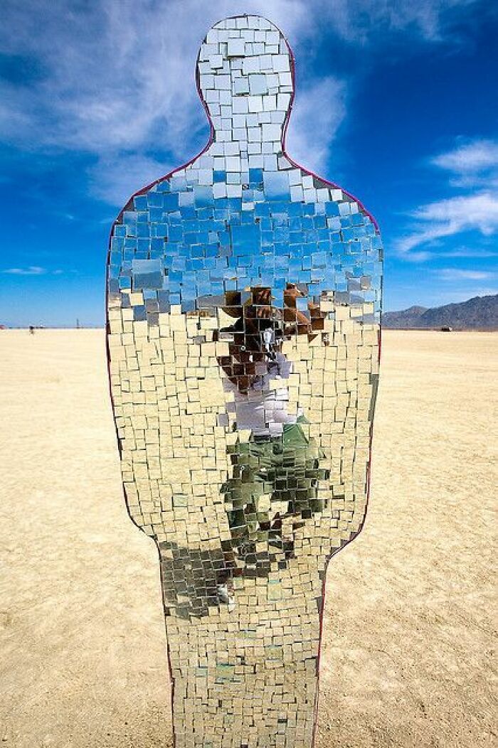 Mirror mosaic sculpture reflecting a person on a desert landscape, creating a trippy picture with fragmented reality effects.