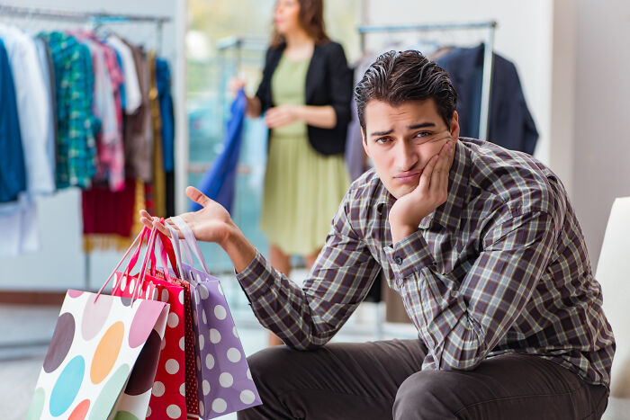 Man looking embarrassed while holding shopping bags in a clothing store, capturing awkward moments others didn’t see.