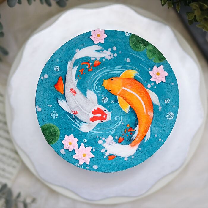 Round cake decorated with masterfully crafted koi fish and water lilies, showcasing detailed and creative cake art.