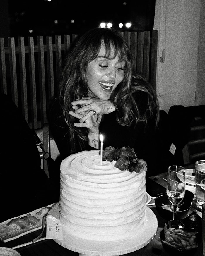 Miley Cyrus smiling at a cake with a candle, celebrating with engagement and mixed reactions about age. Miley Cyrus smiling at a cake with a candle, celebrating with engagement and mixed reactions about age.