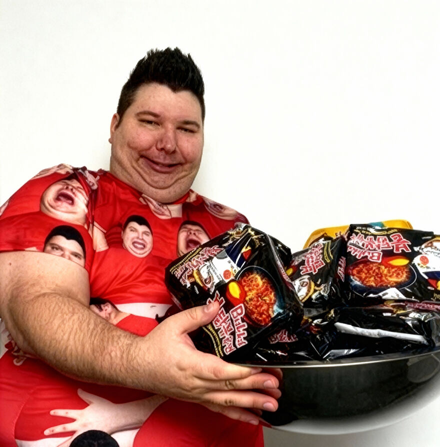 Nikocado Avocado holding a bowl of instant noodles, smiling and wearing a red shirt with multiple faces printed. Nikocado Avocado holding a bowl of instant noodles, smiling and wearing a red shirt with multiple faces printed.