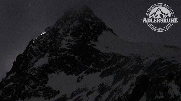 Snowy peak of Austria’s highest mountain at night with climbers' lights and Adlersruhe emblem in the sky corner. Snowy peak of Austria’s highest mountain at night with climbers' lights and Adlersruhe emblem in the sky corner.