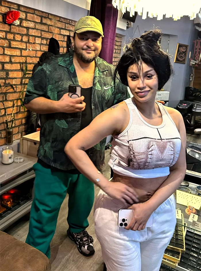 Cardi B posing in casual wear after getting new neck and back piercings with a man taking a photo in the background.