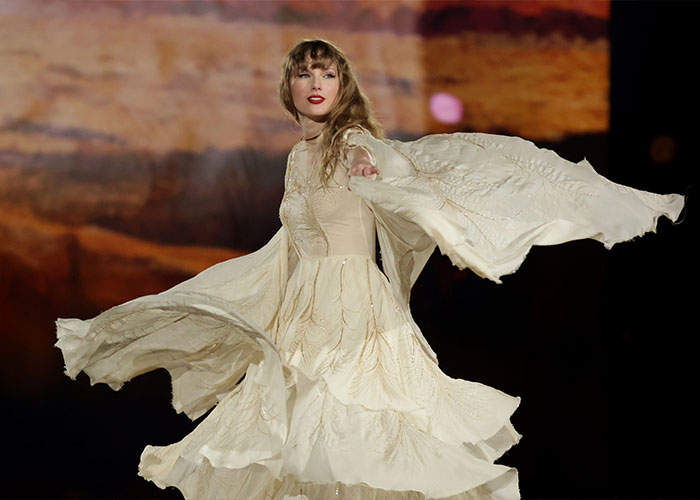 Taylor Swift performing on stage wearing a flowing cream dress amid false claims of coded white-nationalist messages. Taylor Swift performing on stage wearing a flowing cream dress amid false claims of coded white-nationalist messages.