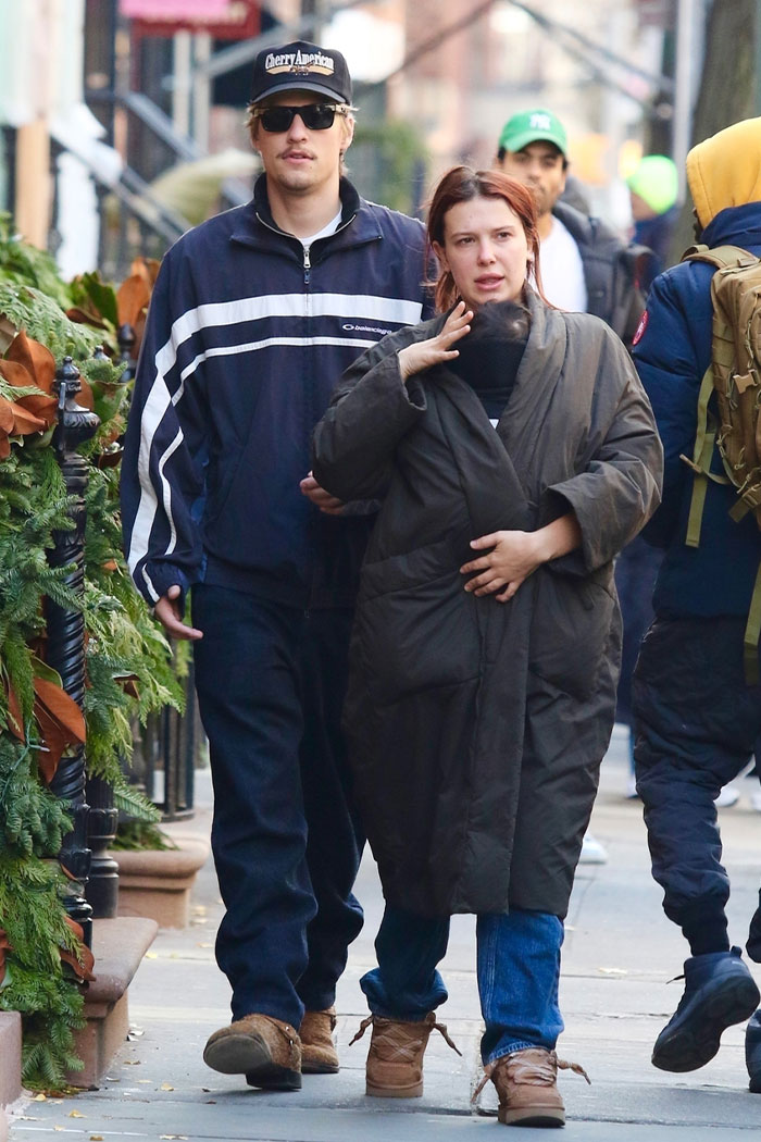 Millie Bobby Brown walking outdoors with arm injury, fueling fan theories about Jake Bongiovi&rsquo;s control and relationship.