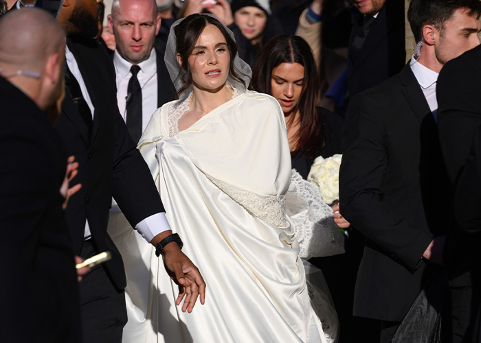 Bride wearing a satin bed sheet style dress surrounded by guests and security at a high-profile wedding event. Bride wearing a satin bed sheet style dress surrounded by guests and security at a high-profile wedding event.