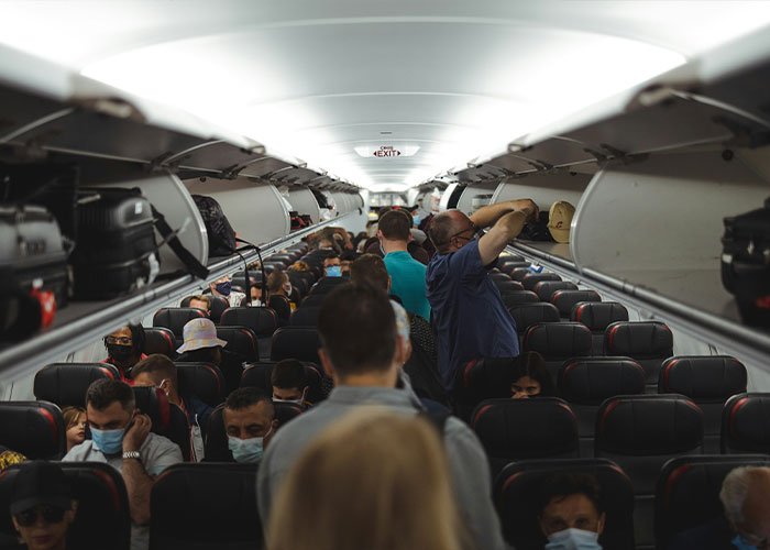 Crowded airplane interior with passengers seated and some standing, illustrating a tense flight experience involving seat switching conflict.