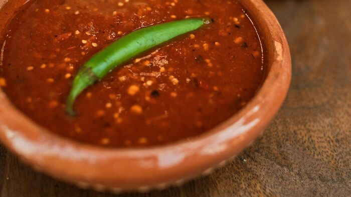 Close-up of a clay bowl with spicy red salsa and a green chili, illustrating ambiguous situations to cast fault or right.