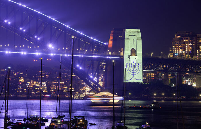 Sydney Harbour Bridge at night with city lights and boats, highlighting public space amid New Year&rsquo;s Eve controversy.