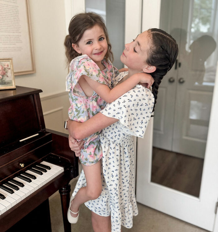 Two young girls embracing near a piano, representing influencer's daughter passing away at Christmas. Two young girls embracing near a piano, representing influencer's daughter passing away at Christmas.