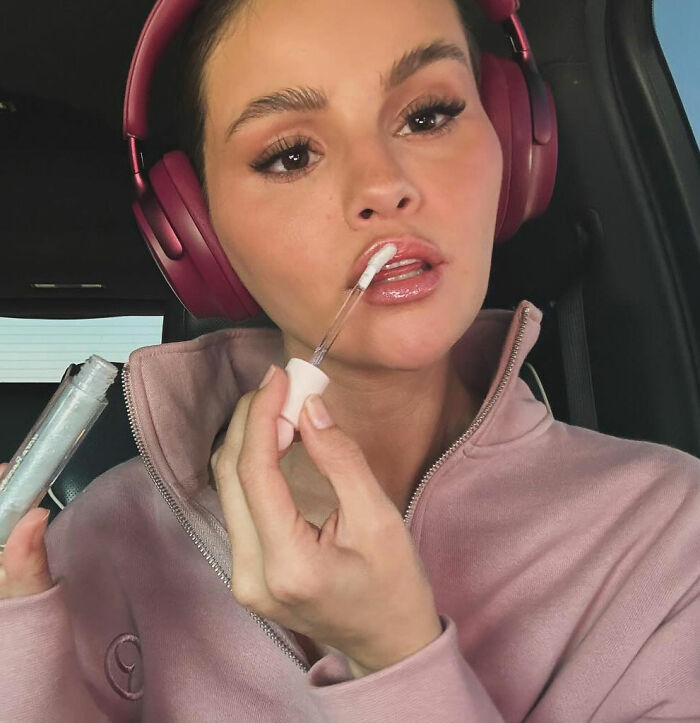 Selena Gomez applying lip gloss wearing headphones in a car, related to fan question about how she shaves her mustache. Selena Gomez applying lip gloss wearing headphones in a car, related to fan question about how she shaves her mustache.