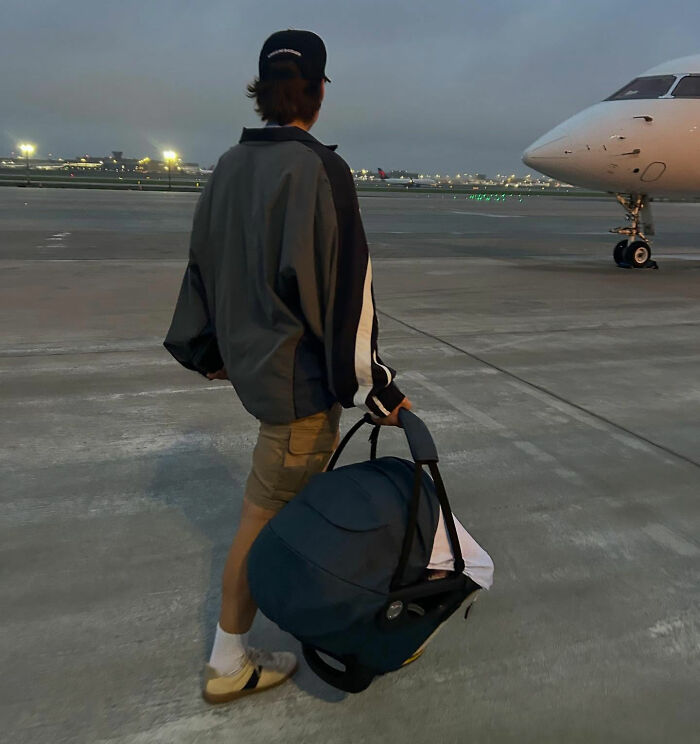 Person carrying a car seat at an airport tarmac at dusk, related to viral theory about Millie Bobby Brown's newborn daughter. Person carrying a car seat at an airport tarmac at dusk, related to viral theory about Millie Bobby Brown's newborn daughter.