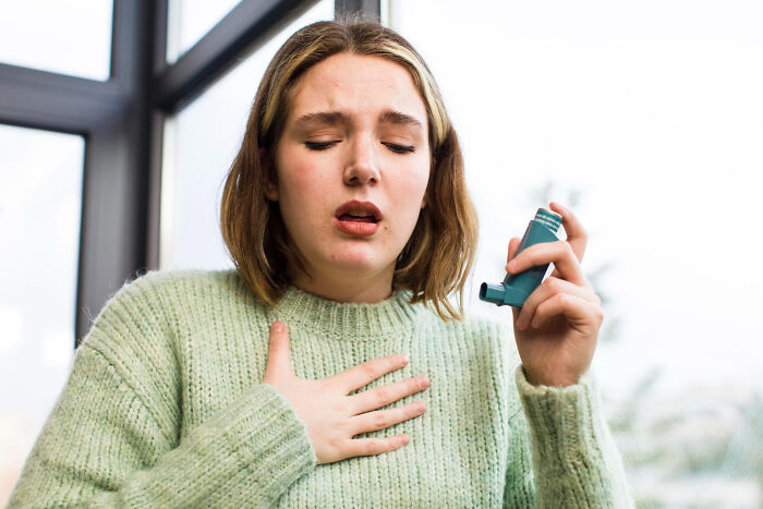 Young woman holding an inhaler and clutching her chest, illustrating a strange and specific kid's insult concept.
